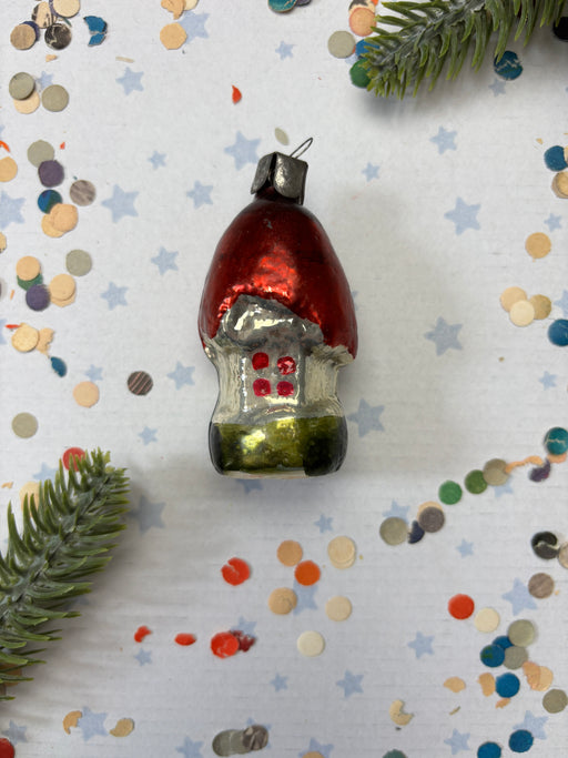 A red ornament with a green base is placed on a white background, surrounded by scattered confetti and a sprig of greenery.