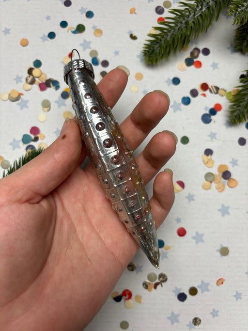 A hand holding a silver ornament with a pointed end, surrounded by colorful confetti on a white background.