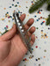 A hand holding a silver ornament with a pointed end, surrounded by colorful confetti on a white background.