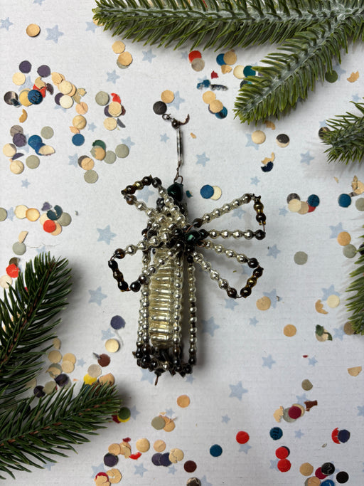 a silver and black beaded ornament with a spider-like design, surrounded by Christmas confetti and pine branches.