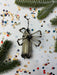 a silver and black beaded ornament with a spider-like design, surrounded by Christmas confetti and pine branches.