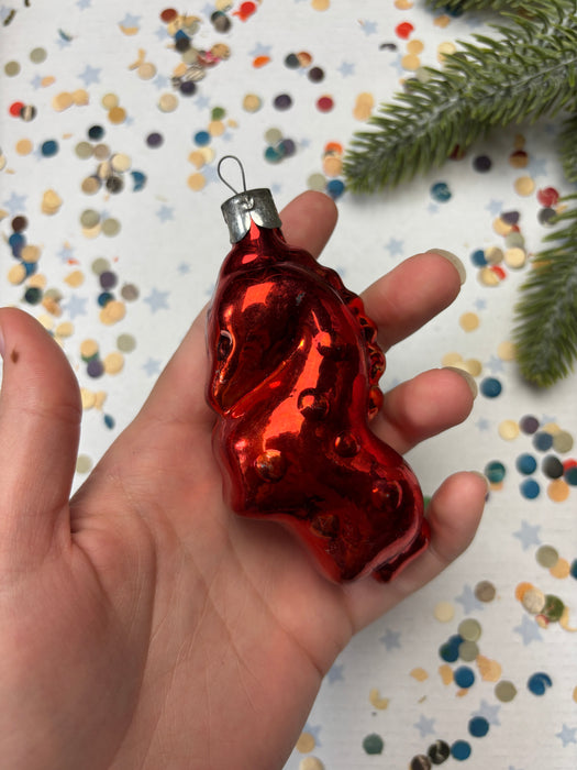 A hand holding a shiny red ornament against a background of colorful confetti.