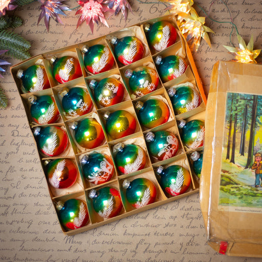 A box filled with colorful Christmas ornaments, including glass baubles and baubles with intricate designs, placed on a wooden surface with a handwritten note and a small picture frame.