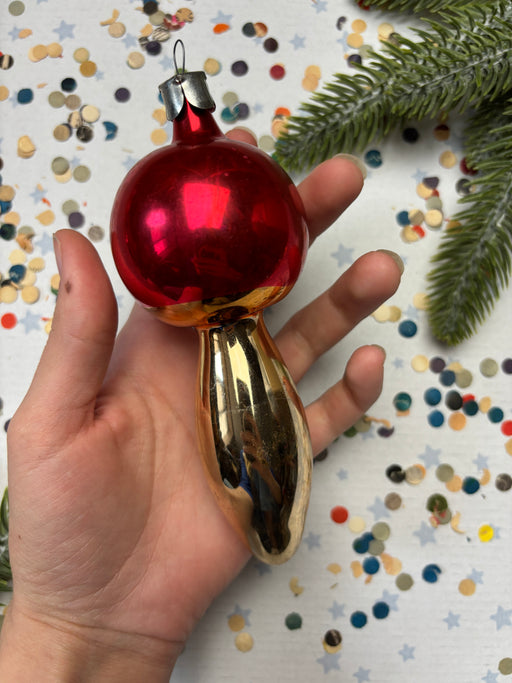 A hand holding a red ornament with a gold base, surrounded by colorful confetti on a white background.