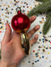 A hand holding a red ornament with a gold base, surrounded by colorful confetti on a white background.