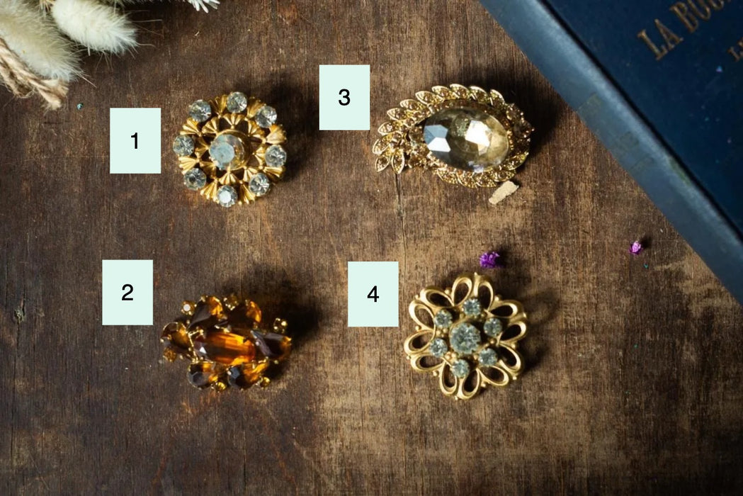 a collection of ornate brooches and jewelry pieces, including a large crystal-encrusted brooch, a smaller brooch with a floral design, and a pair of brooches with intricate designs.