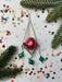 a festive scene with Christmas decorations, including a red ornament, green ornaments, and confetti scattered on a white background.