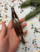 A hand holding a shiny, metallic object against a background of colorful confetti and a pine tree branch.