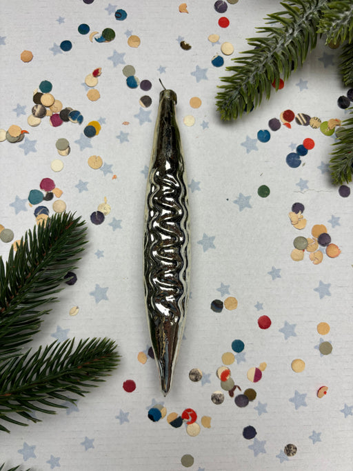 a metallic ornament with a wavy design, surrounded by colorful confetti and pine branches.