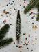 a metallic ornament with a wavy design, surrounded by colorful confetti and pine branches.