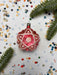 A red star-shaped ornament with a silver star at the center is surrounded by pine branches, confetti, and small star-shaped decorations on a white background.