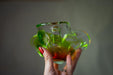 A hand holding a green glass vase with a red handle.