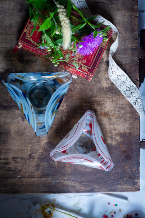 two glass vases with different designs, placed on a wooden surface. There is also a red book and a white lace ribbon in the background.