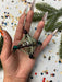 A hand holding a beaded necklace with a star-shaped pendant, surrounded by confetti and a pine tree branch.