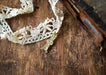 A delicate white lace trim and a small golden rabbit charm are placed on a wooden surface.