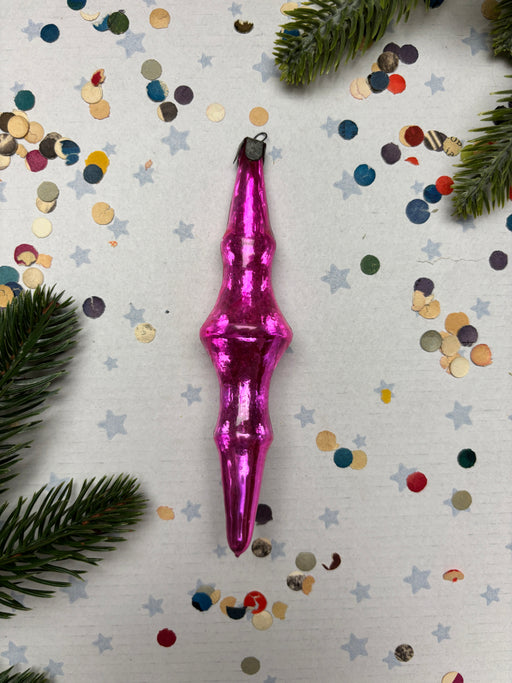 A pink ornament is placed on a white background with scattered confetti and pine branches.
