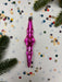 A pink ornament is placed on a white background with scattered confetti and pine branches.