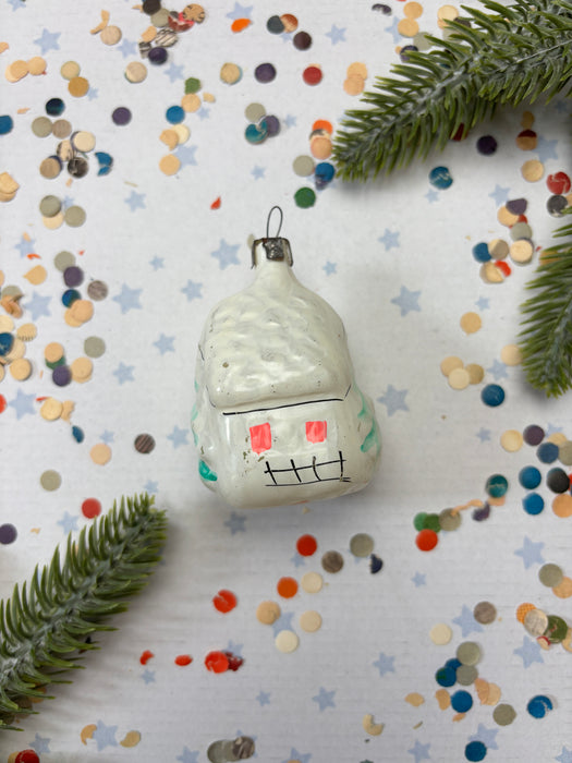 a small white ornament with red and black markings, surrounded by colorful confetti and green pine branches.