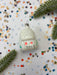 a small white ornament with red and black markings, surrounded by colorful confetti and green pine branches.