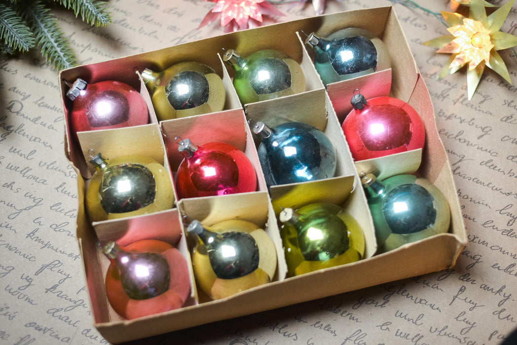 A cardboard box filled with a dozen colorful Christmas ornaments, including red, green, blue, and yellow balls, arranged neatly in the box.