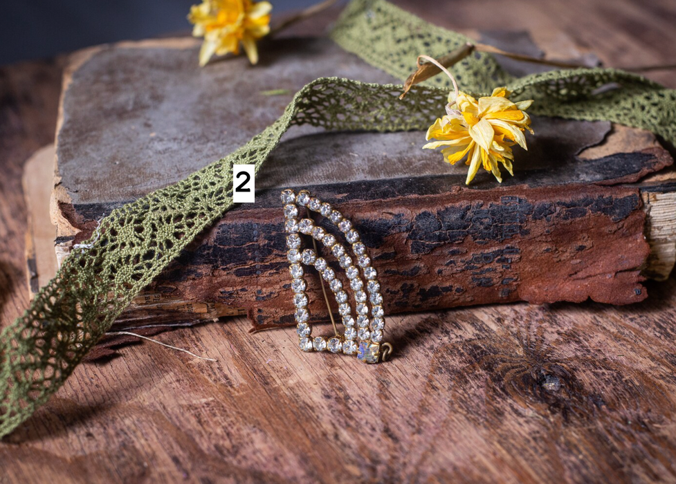 a vintage book with a decorative brooch on top, a yellow flower, and a green lace ribbon on a wooden surface.