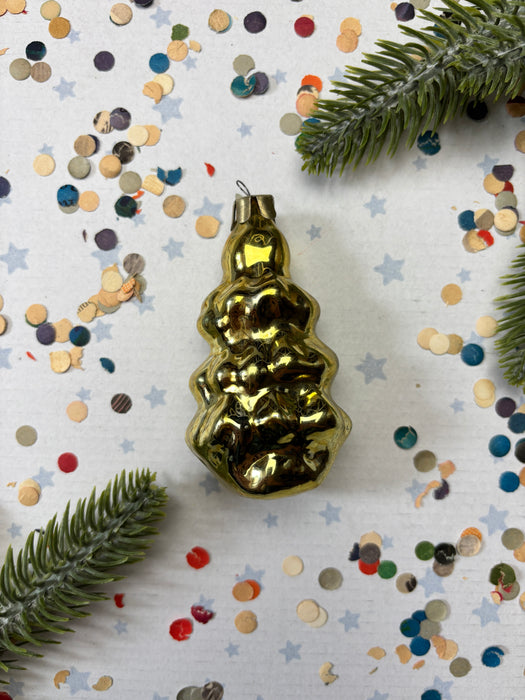 a golden ornament with a star-shaped design, surrounded by confetti and a sprig of greenery.