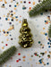 a golden ornament with a star-shaped design, surrounded by confetti and a sprig of greenery.