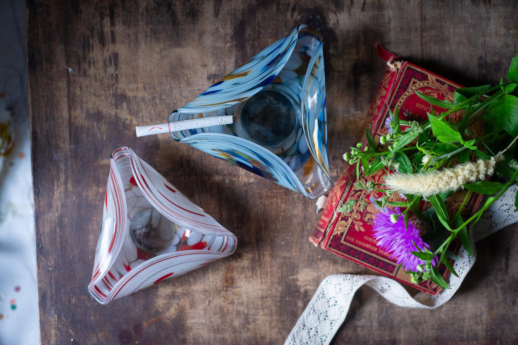a wooden table with two glass ashtrays, a red book with a white lace ribbon, and a purple flower.