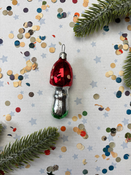 A red ornament with white polka dots is placed on a white background, surrounded by colorful confetti and green pine branches.