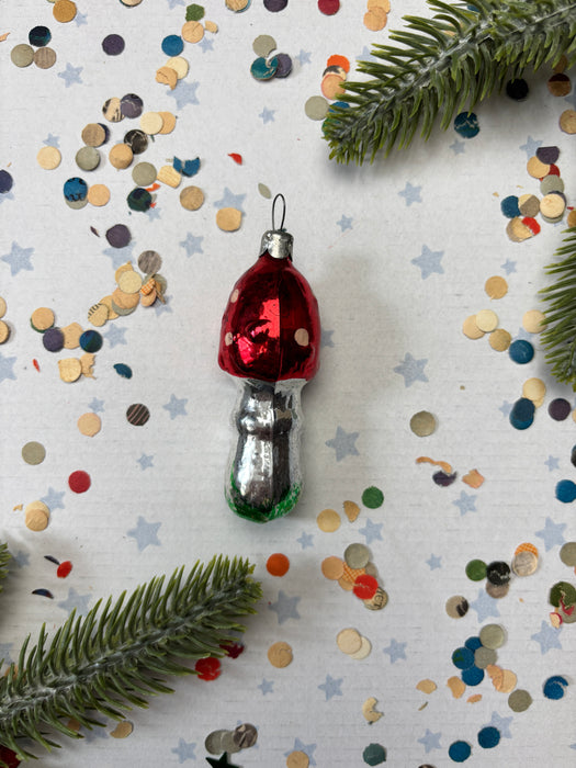 A red ornament with white polka dots is placed on a white background, surrounded by colorful confetti and green pine branches.
