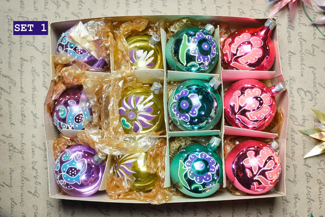 A set of colorful Christmas ornaments in a cardboard box, with various designs and colors including red, green, blue, and purple.