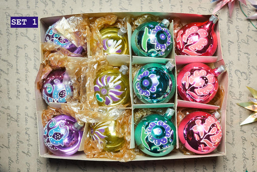 A set of colorful Christmas ornaments in a cardboard box, with various designs and colors including red, green, blue, and purple.