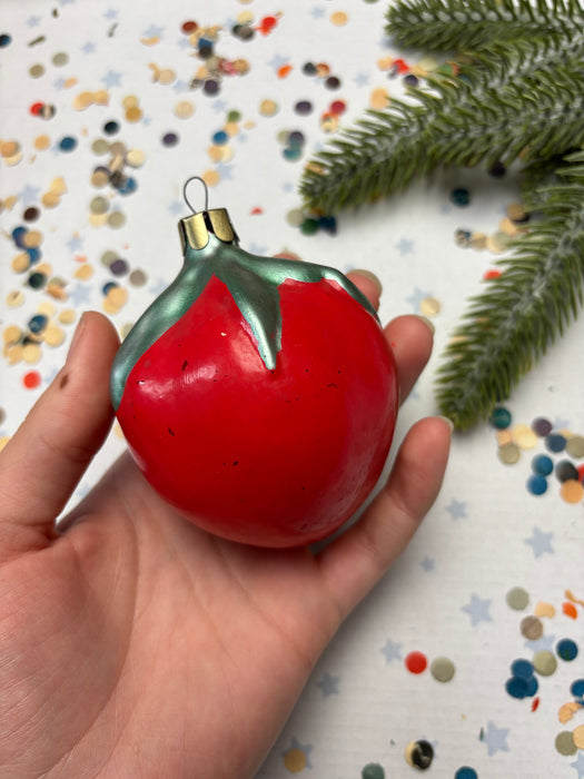 A hand holding a red ornament with a green stem, surrounded by colorful confetti on a white background.