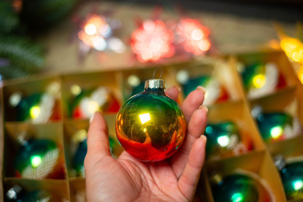 A hand holding a shiny, multicolored ornament against a blurred background of other ornaments.