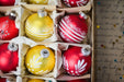 A close-up view of a collection of colorful Christmas ornaments, including red, yellow, and white ornaments, arranged in a box.