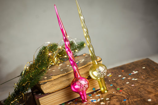two colorful glass ornaments, one pink and one gold, placed on top of a stack of books and surrounded by a festive garland and confetti.