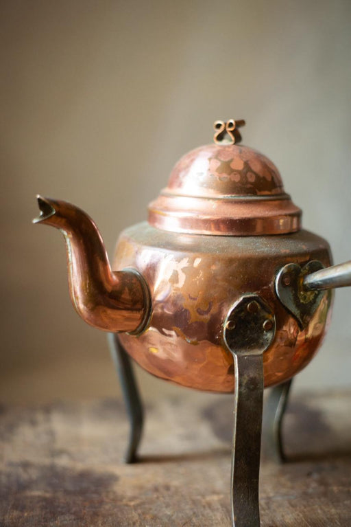 A copper-colored kettle with a dome-shaped lid and a spout, standing on a wooden surface.