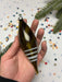 A hand holding a green glass ornament with white stripes, surrounded by colorful confetti and a pine tree branch.