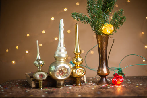 a collection of vintage ornaments, including a Christmas tree topper, a small glass ornament, and a brass ornament, arranged on a wooden surface. A small red flower is also present in the scene.