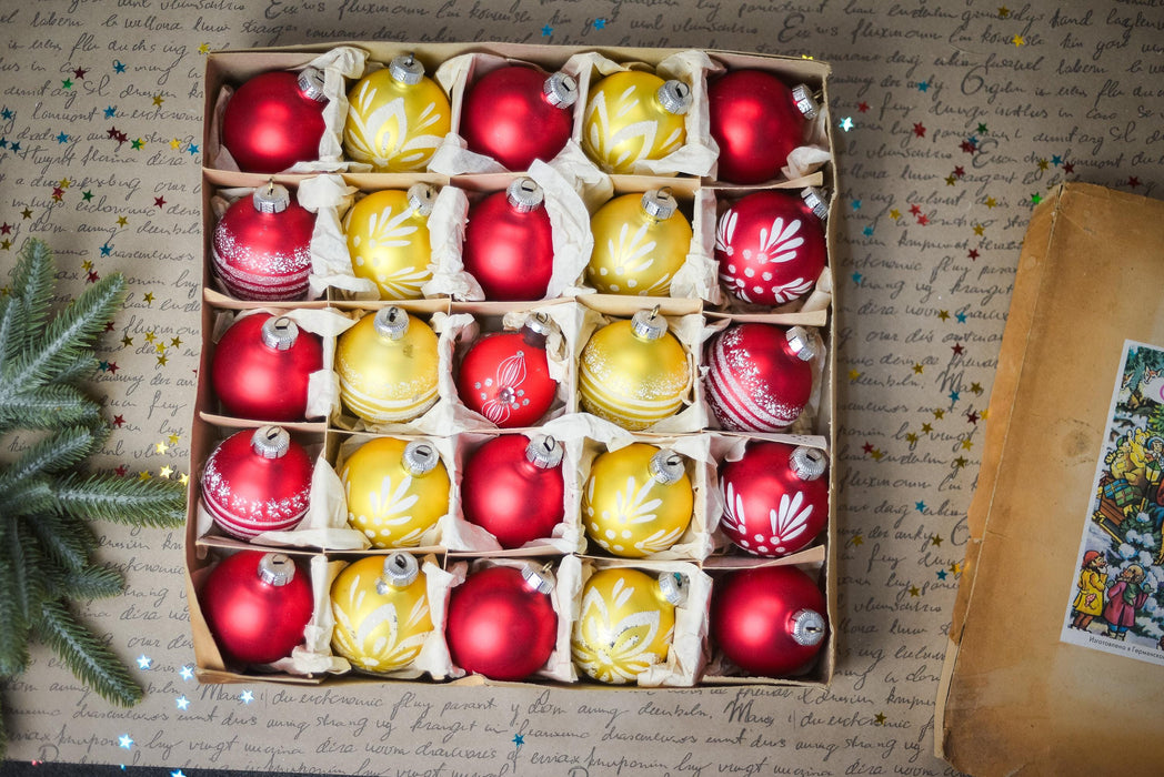 A box filled with red and yellow Christmas ornaments, arranged neatly in rows.