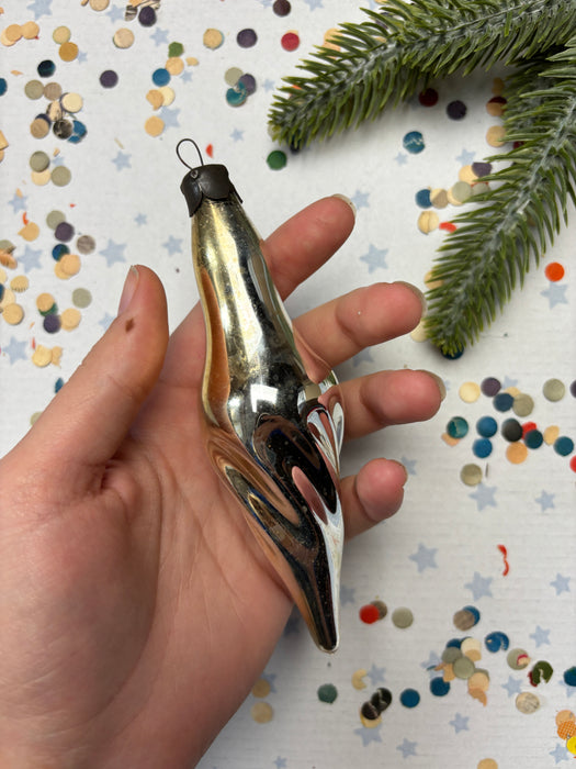A hand holding a shiny, metallic ornament against a background of colorful confetti and a green pine branch.
