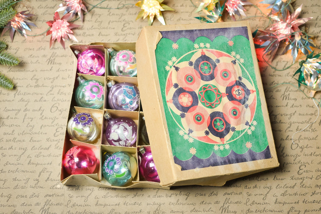 a cardboard box filled with colorful glass ornaments, including a variety of shapes and designs, placed on a surface with scattered decorative elements.
