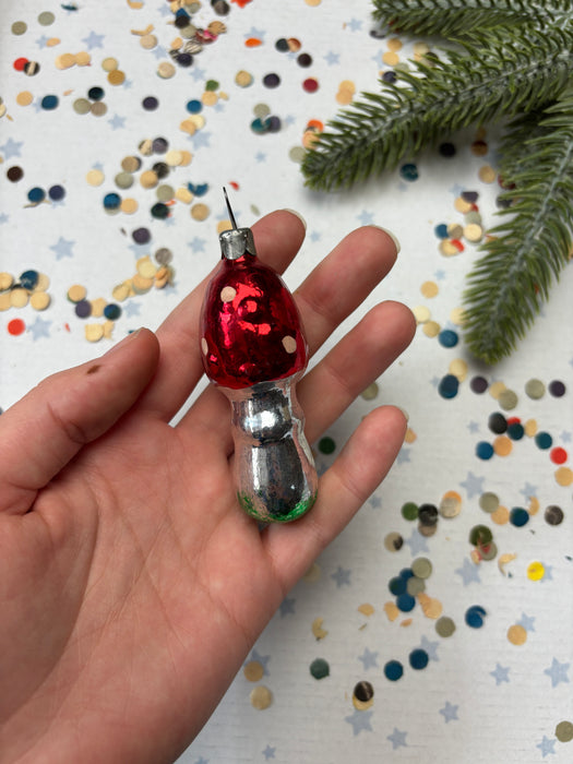 A hand holding a red ornament with a silver base, surrounded by colorful confetti on a white background.