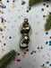 A shiny silver ornament is placed on a white background, surrounded by colorful confetti and a sprig of greenery.