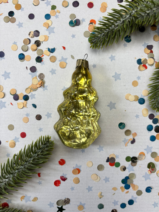 a golden ornament with a wavy shape, surrounded by colorful confetti and green pine branches.