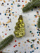a golden ornament with a wavy shape, surrounded by colorful confetti and green pine branches.