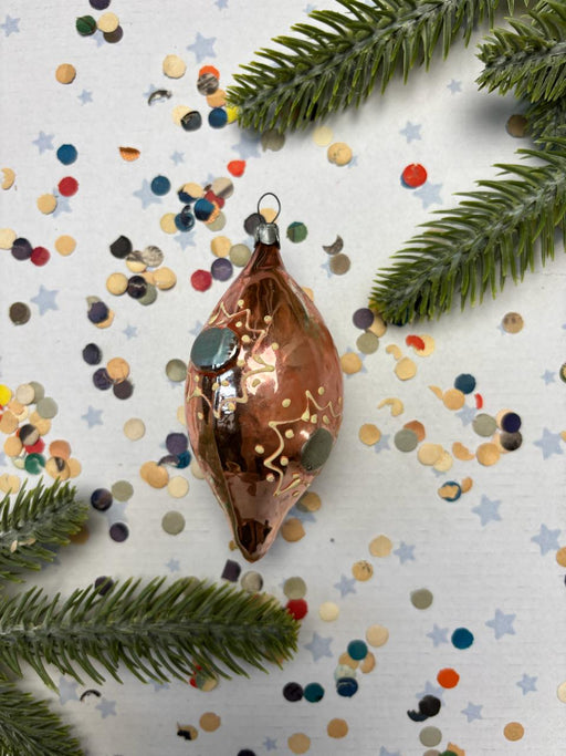 a Christmas ornament with a copper-colored design, surrounded by colorful confetti and pine branches.