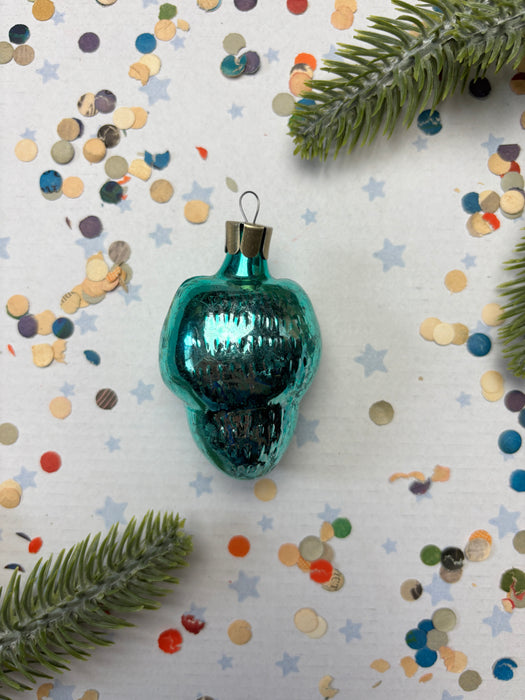 A turquoise Christmas ornament is surrounded by colorful confetti and a sprig of greenery on a white background.