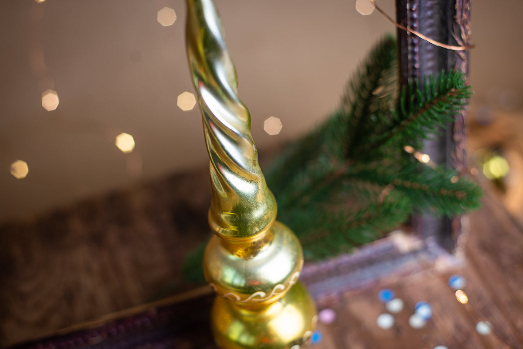 A golden Christmas ornament with a spiral design sits on a wooden surface, surrounded by a blurred background of twinkling lights.