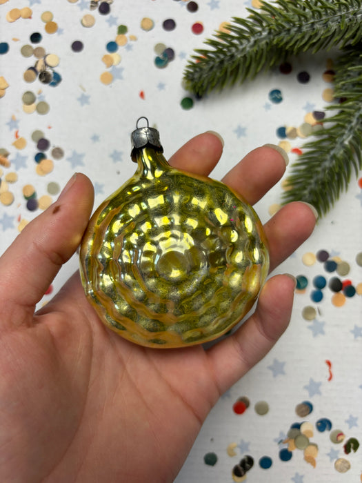 A hand holding a shiny, golden-colored ornament against a background of colorful confetti.